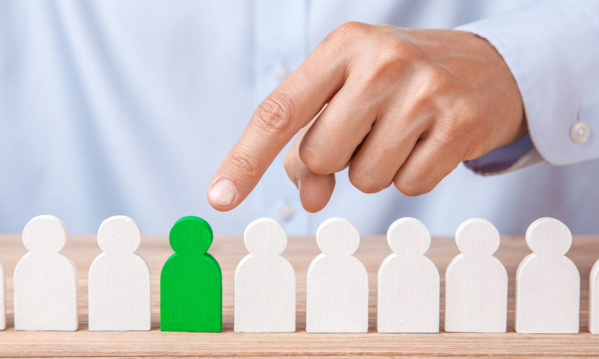 Featured image for "Best Piano Lessons" page on Piano Lessons -dotcom depicting man in nice business shirt pointing to the lone green wooden figure in a row of white wooden figures.